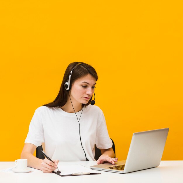 Mujer que trabaja en el escritorio mientras usa auriculares y mira la computadora portátil