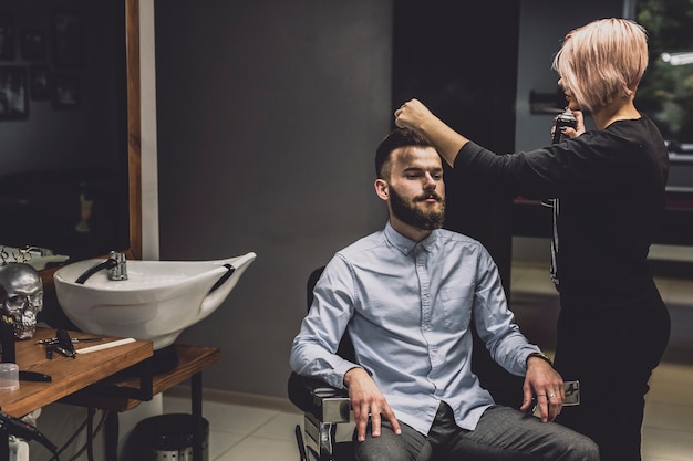 Foto gratuita mujer que usa el aerosol en cliente en barbería