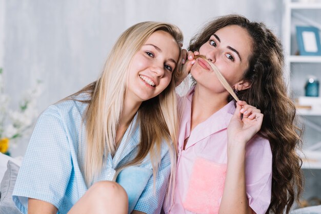 Mujer que usa el cabello de su amiga sonriente para hacer un bigote falso