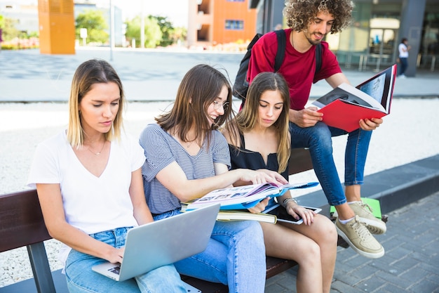 Mujer que usa la computadora portátil cerca de amigos con los libros de texto