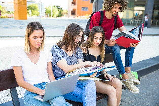 Mujer que usa la computadora portátil cerca de amigos con los libros de texto