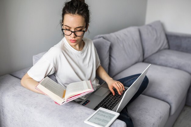 Mujer que usa la computadora portátil y el libro de lectura