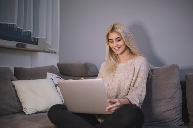 Mujer que usa la computadora portátil en el sofá