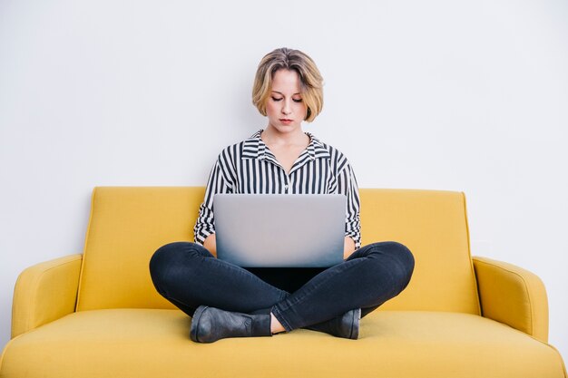 Mujer que usa la computadora portátil en el sofá