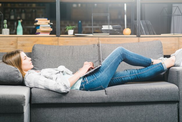 Mujer que usa la computadora portátil en el sofá