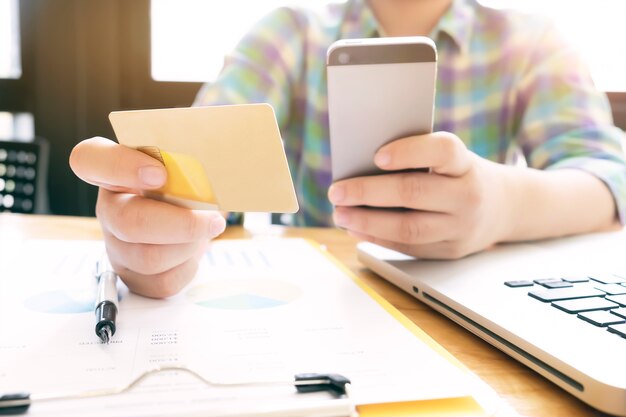 Mujer que usa la computadora portátil y el teléfono móvil a las compras en línea ya paga por de la tarjeta de crédito.