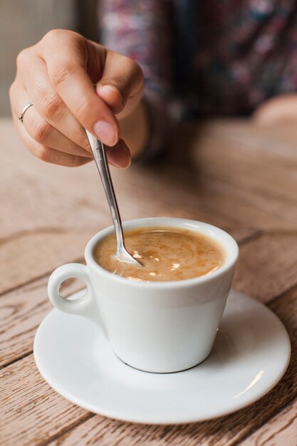 Mujer que usa una cuchara para revolver el café en una taza blanca sobre la mesa