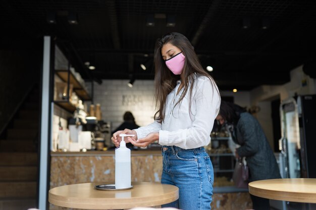 Mujer que usa gel desinfectante limpia las manos del virus del coronavirus en el café