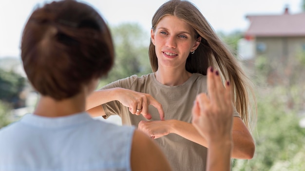 Mujer que usa el lenguaje de señas mientras está al aire libre para conversar con su amiga
