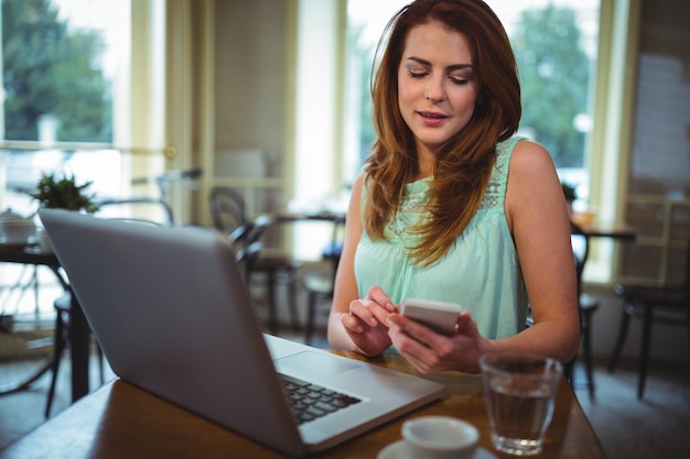 Mujer que usa el ordenador portátil y el teléfono móvil