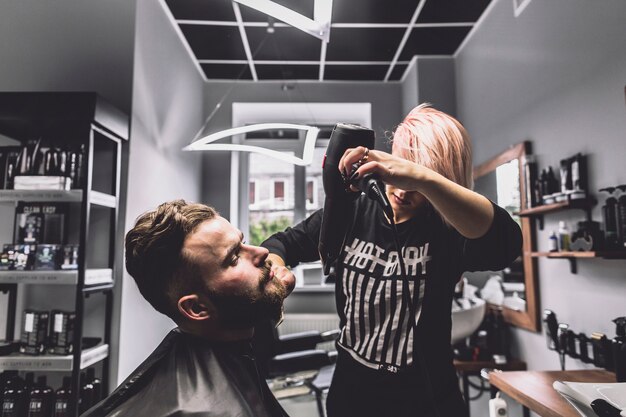 Mujer que usa el secador en la barba del hombre