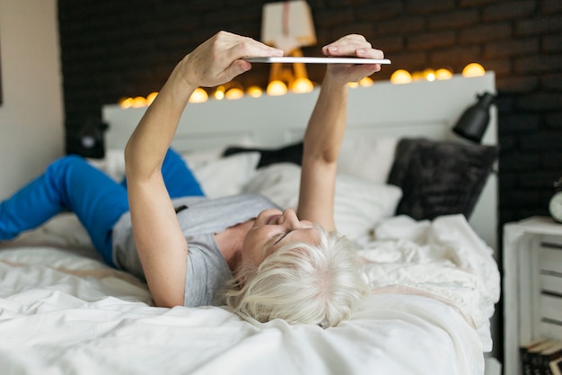 Mujer que usa la tableta en la cama