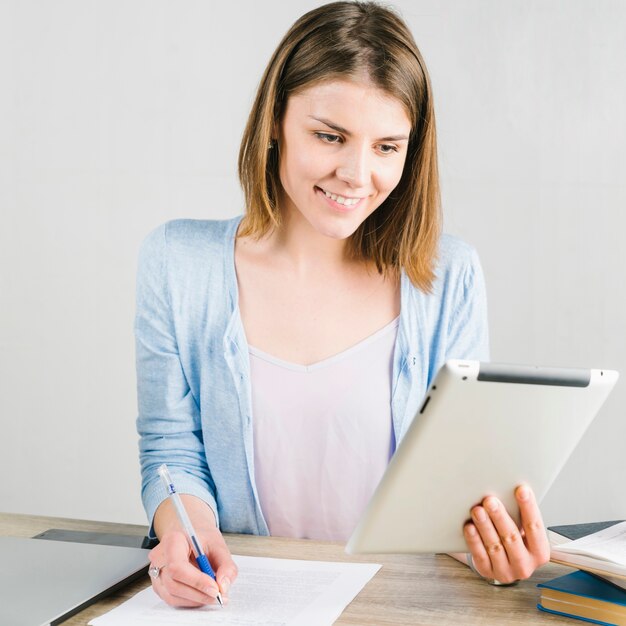 Mujer que usa la tableta y haciendo notas