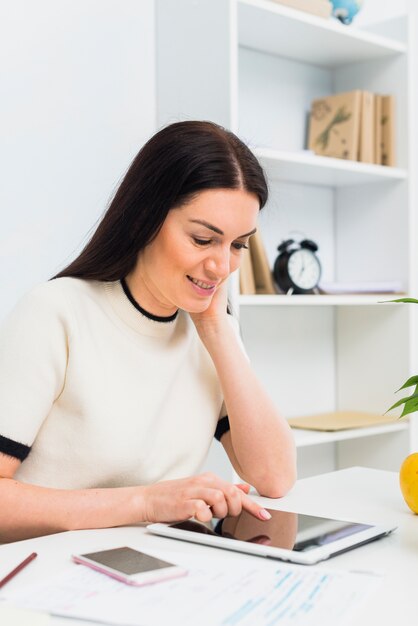 Mujer que usa la tableta en la mesa en la oficina