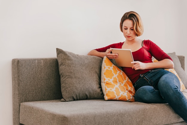 Mujer que usa la tableta en el sofá