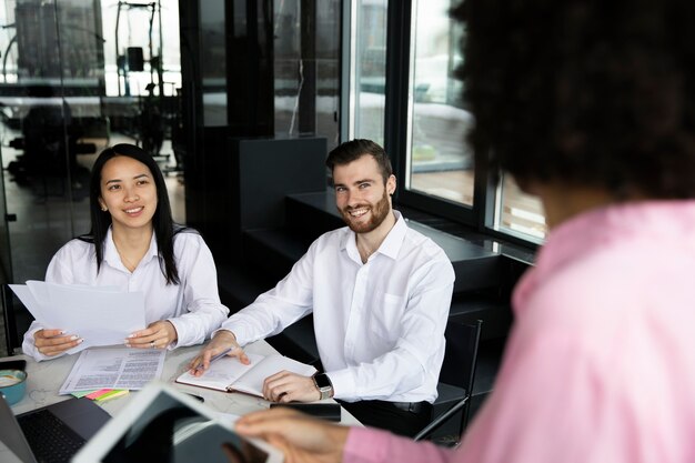 Mujer que usa una tableta para trabajar mientras sus colegas usan una computadora portátil y documentos