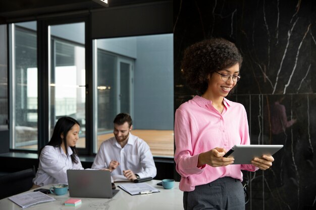 Mujer que usa una tableta para trabajar mientras sus colegas usan una computadora portátil