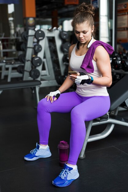 Mujer que usa el teléfono inteligente en el banco en el gimnasio