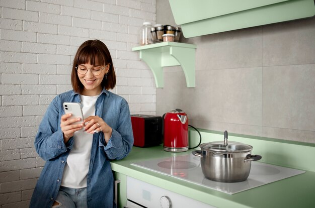 Mujer que usa un teléfono inteligente en una cocina verde