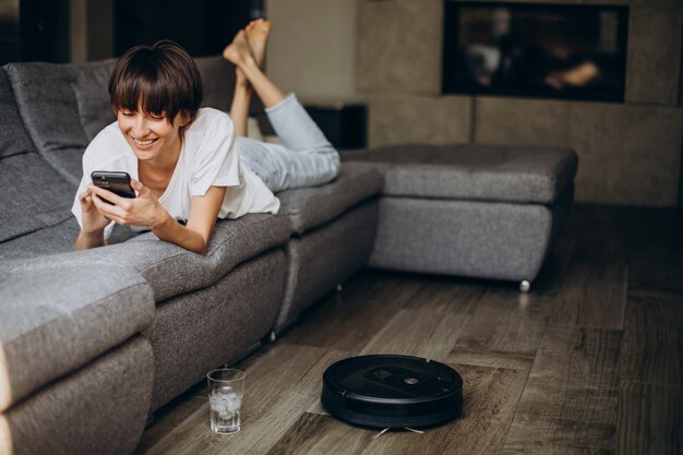 Mujer que usa el teléfono mientras el robot aspirador limpia el piso