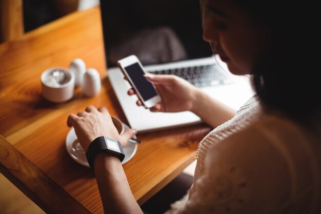 Mujer que usa el teléfono móvil mientras toma una taza de café