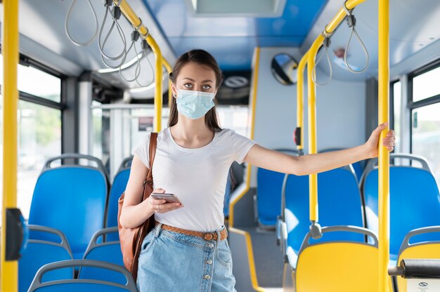 Mujer que viaja en autobús público con smartphone mientras usa máscara médica para protección