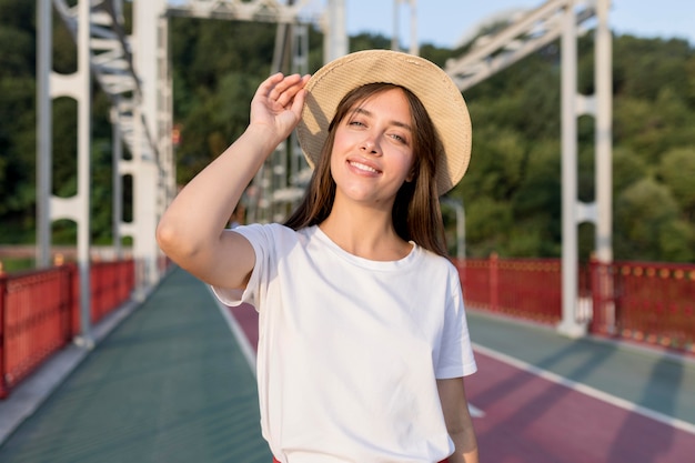 Foto gratuita mujer que viaja sonriente en puente con sombrero