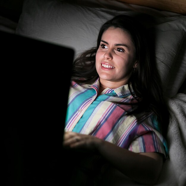 Mujer quedándose en la cama y trabajando en la computadora portátil