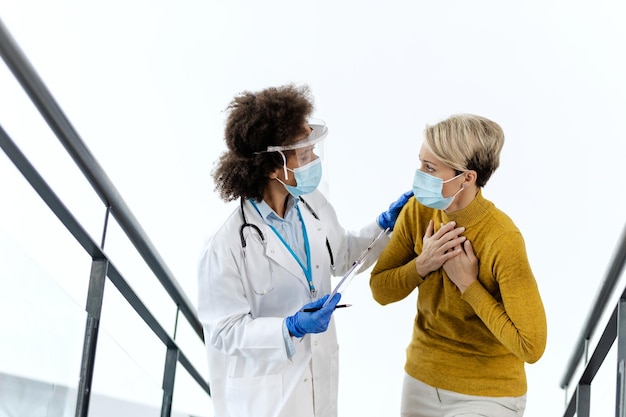 Mujer quejándose de dolor en el pecho mientras habla con una doctora en la clínica médica