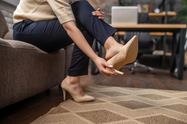 Mujer quitándose elegantes zapatos de tacón alto en la alfombra