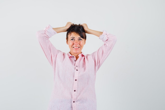 Mujer rasgando su cabello con camisa rosa y mirando nostálgico, vista frontal.