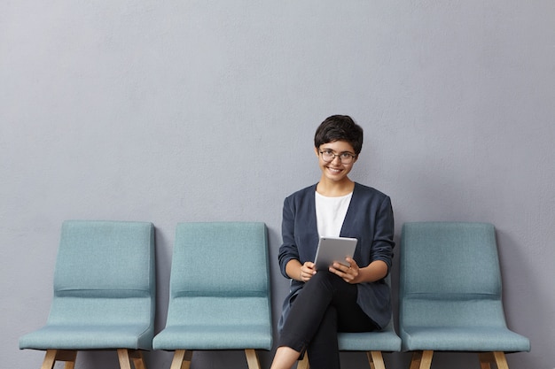 Mujer de raza mixta de aspecto agradable tiene un peinado corto de moda, usa gafas y chaqueta formal, viene a la entrevista de trabajo,