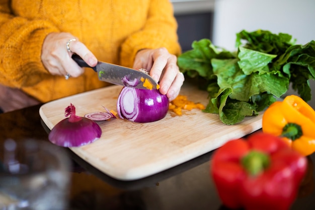 Mujer rebanar cebolla roja y cocinar en una cocina