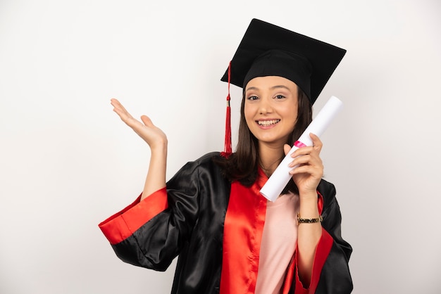 Mujer recién graduada con diploma posando sobre fondo blanco.