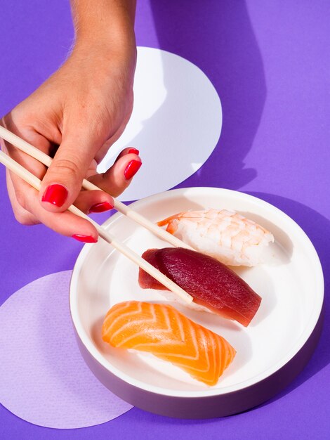 Mujer recogiendo un atún sushi con palillos de la placa