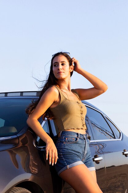 Mujer recostada en el coche y posando bajo el sol