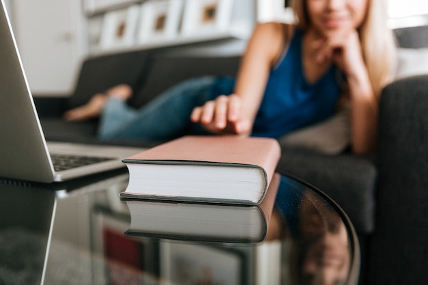 Mujer recostada en el sofá y tomando el libro de la mesa