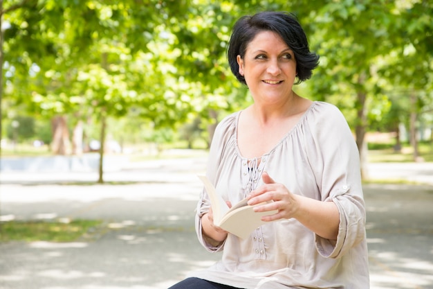 Mujer relajada feliz que pasa las páginas del libro al aire libre