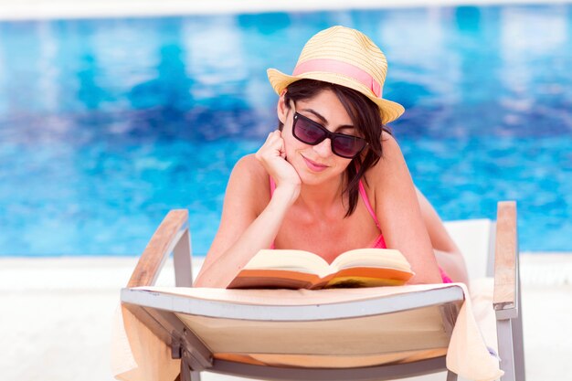 Mujer relajada leyendo un libro con la piscina de fondo