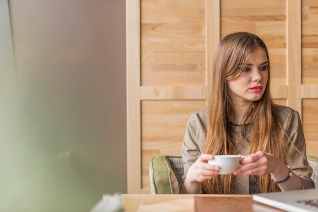 Mujer relajada con taza de té mirando hacia su portátil