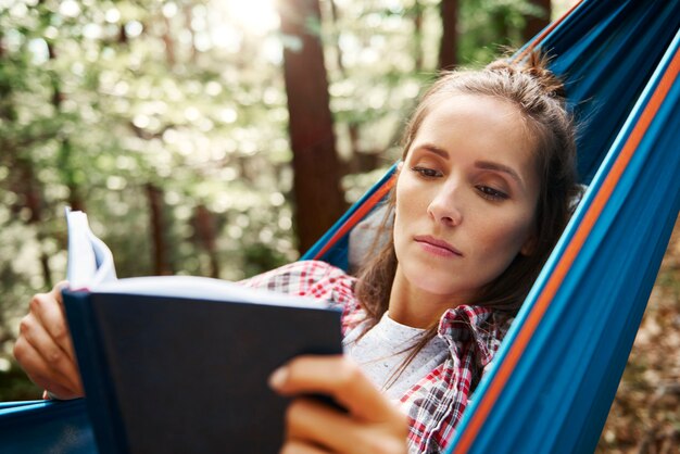 Mujer relajándose en una hamaca y leyendo un libro