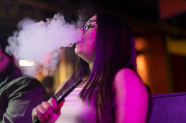 Mujer relajándose vaping de una pipa de agua en un bar.