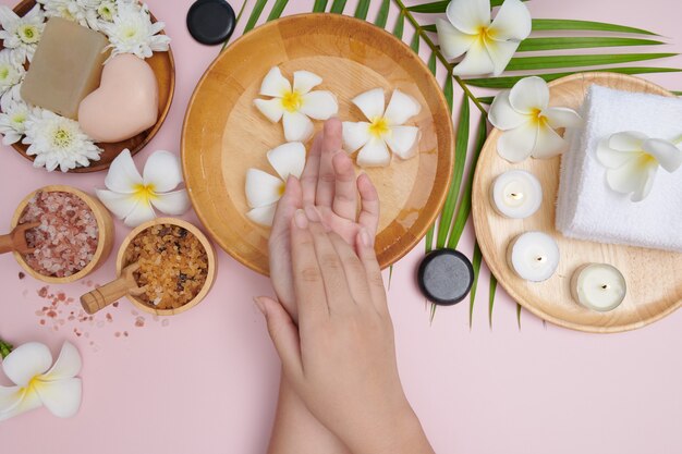 Mujer remojando sus manos en un recipiente con agua y flores, tratamiento de spa y producto para pies femeninos y spa de manos, masaje de guijarros, agua de flores perfumadas y velas, relajación. Endecha plana. vista superior.