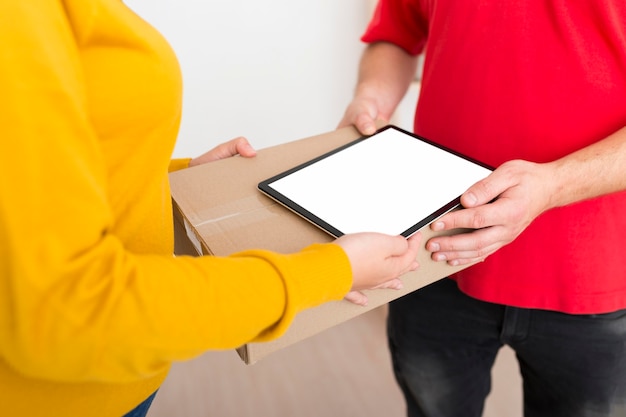 Mujer y repartidor sosteniendo una caja y una tableta de pantalla vacía