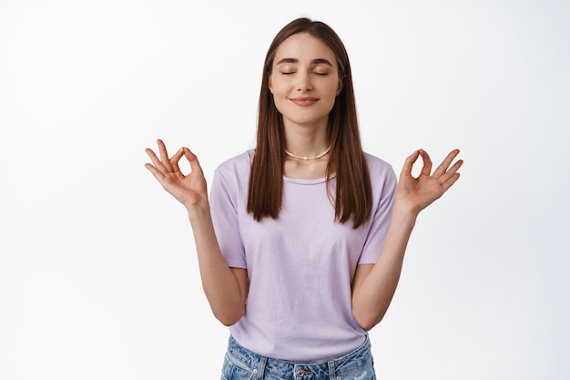 Mujer respirando y meditando pacíficamente, inhala libre y relajada, practica yoga, siéntete aliviada, de pie sobre blanco