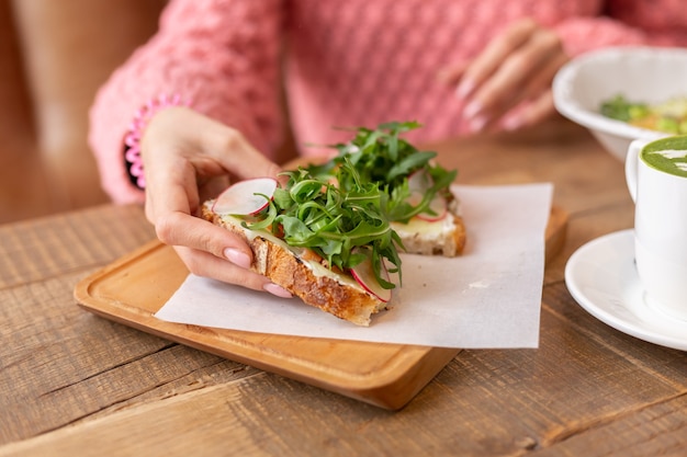 Mujer en un restaurante en un cálido suéter acogedor desayuno saludable con tostadas con rúcula y salmón