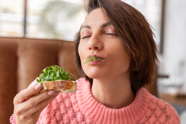 Mujer en un restaurante en un cálido suéter acogedor desayuno saludable con tostadas con rúcula y salmón
