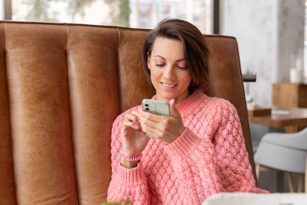 Mujer en un restaurante con un suéter caliente está mirando algo en el teléfono