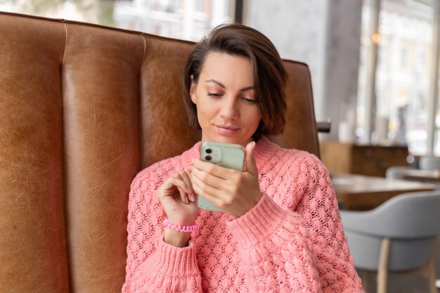 Mujer en un restaurante con un suéter caliente está mirando algo en el teléfono