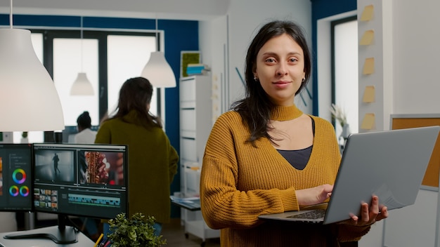 Mujer retocadora mirando a cámara sonriendo trabajando en agencia de medios creativos de pie delante de webc ...